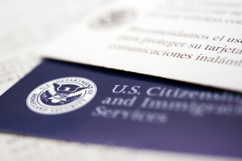 [ai] A close-up view of a U.S. Citizenship and Immigration Services card showing the official seal and text, partially obscured by a white document with text in Spanish.
